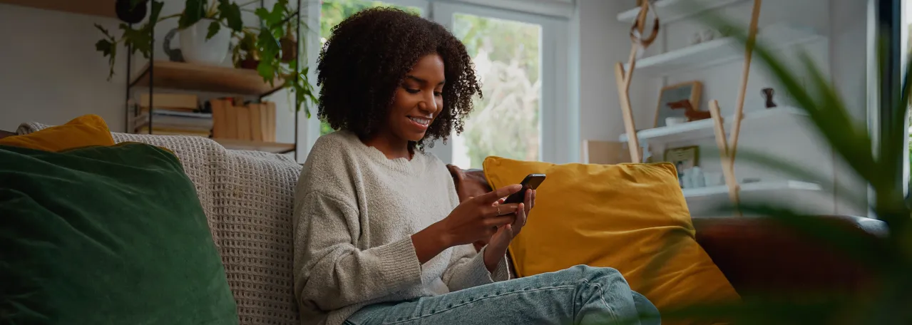 Person sitting on couch with green and yellow pillows in living room while smiling and reading a new business message via WhatsApp