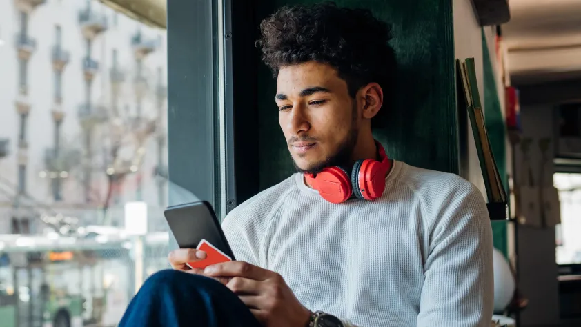 Person sitting on windowsill in a cafe with headphones around their neck while reading a financial services message through WhatsApp on phone