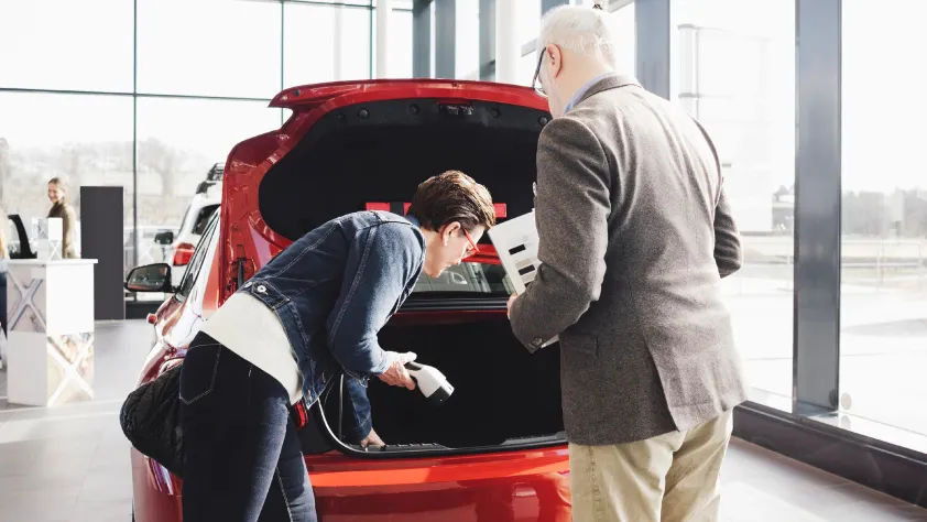 Car salesperson and customer looking inside the trunk of a new red car at a dealership