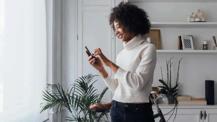 Person standing in living room in front of a bike and plant while reading a personalized business message via WhatsApp