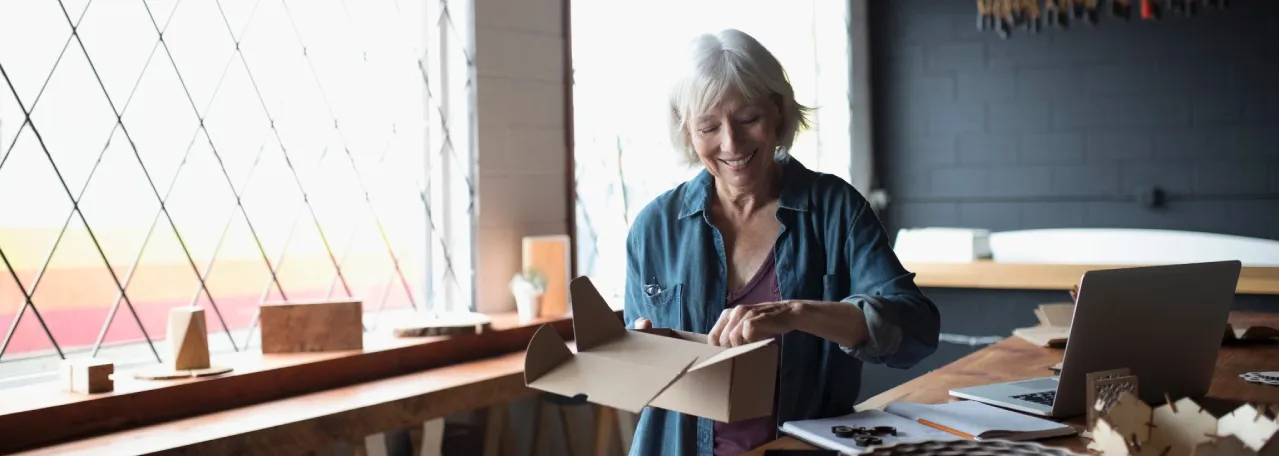 Small business owner standing in studio in front of desk and laptop while packing up a box