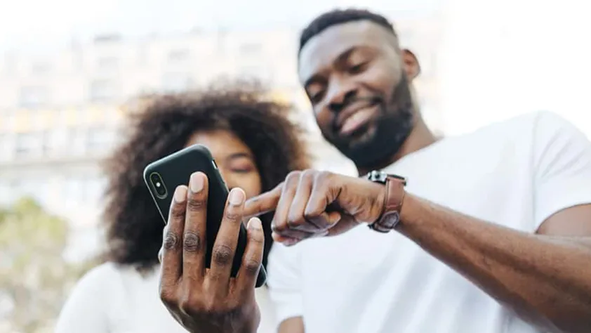 One person standing next to another person who is holding their phone and pointing to the screen