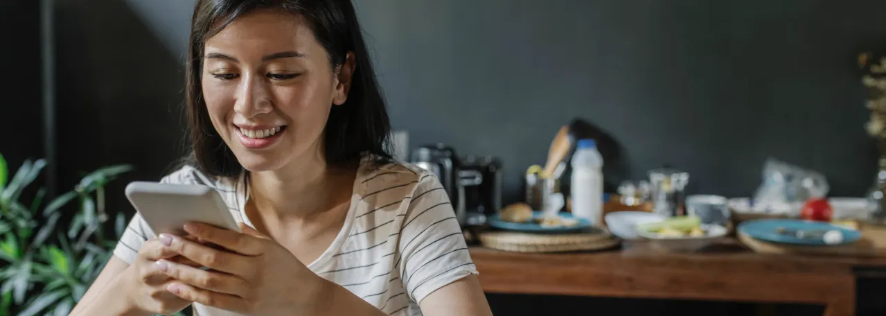 Person sitting in front of dining room table with breakfast food while smiling and reading a financial services message via WhatsApp