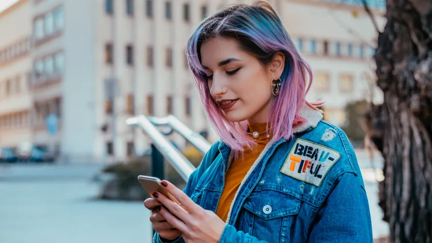 Pessoa em pé na rua usando uma jaqueta jeans. Ela está lendo uma mensagem promocional no WhatsApp no smartphone
