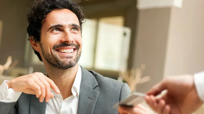 Person in a suit, smiling, while placing a credit card in another person's hand to make a purchase