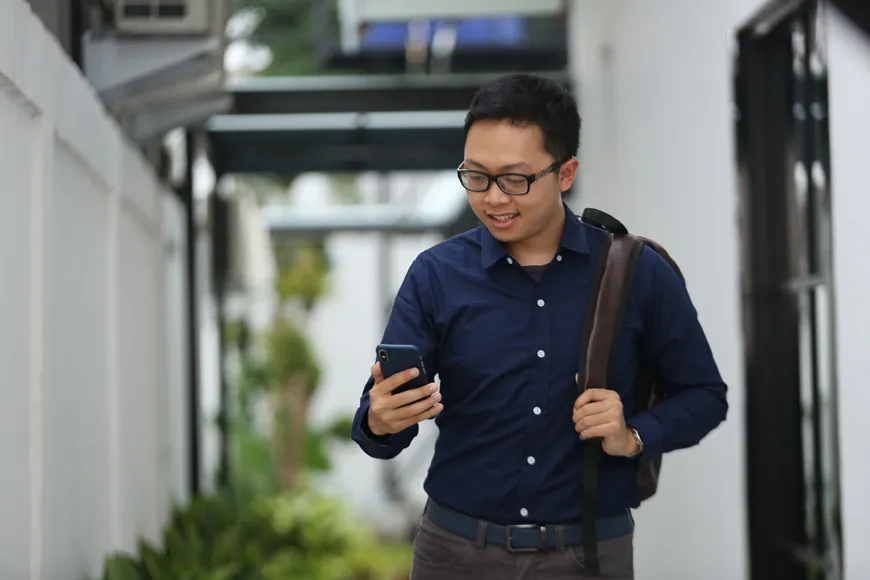 Seorang pria meninggalkan kantor sambil memeriksa ponselnya dengan penuh perhatian.