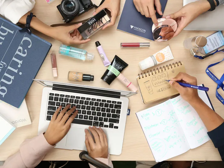 An overhead view of a desk featuring a laptop, beauty products, and notebooks.