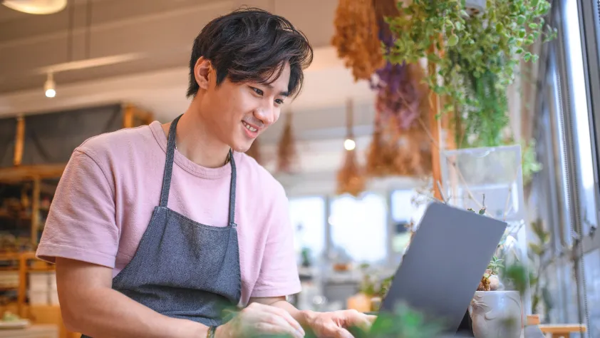 Small business owner in plant shop messaging a new customer on laptop via WhatsApp
