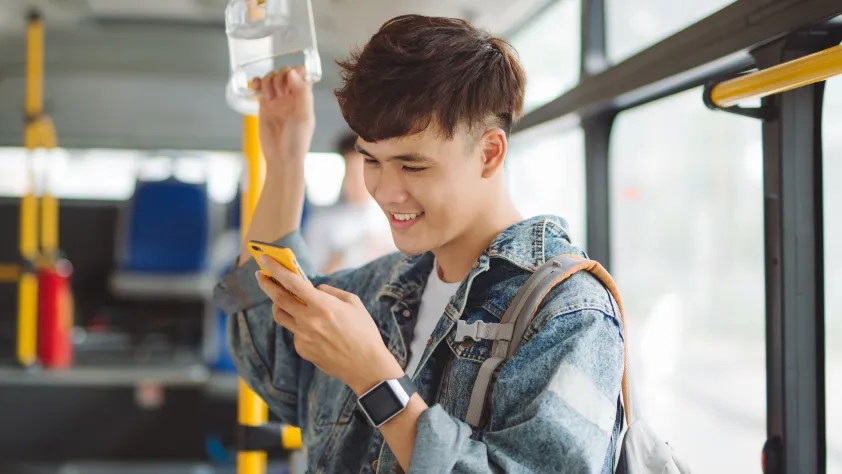 Pessoa em pé no ônibus. Ela sorri ao ler a mensagem de uma empresa pelo WhatsApp no smartphone