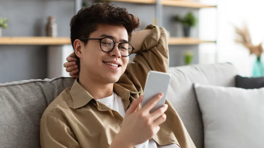 Person sitting on couch in office, wearing glasses and smiling, while reading a WhatsApp message from Akulaku