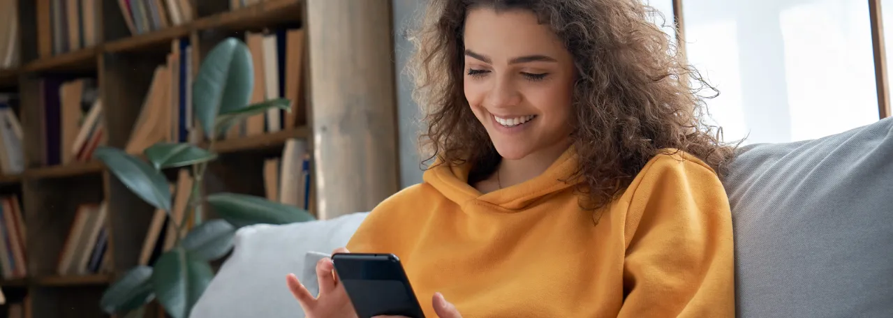 Person sitting on a gray couch while wearing a yellow sweatshirt and making a purchase from a WhatsApp business message