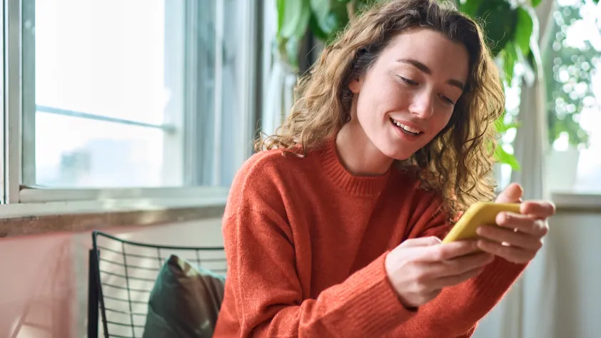 Person sitting on chair in living room while viewing their recent transactions on phone