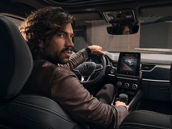 A man seated on the driver's seat of a Renault car.
