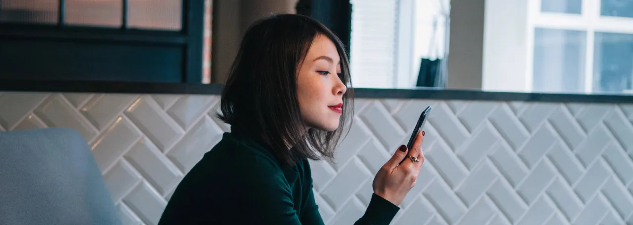 Person sitting in office against white backsplash, wearing a dark colored shirt while looking at phone