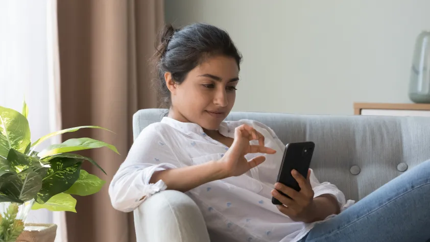 Person sitting in living room on a light blue couch, wearing a white shirt and blue jeans. They are interacting with an ad that clicks to WhatsApp.