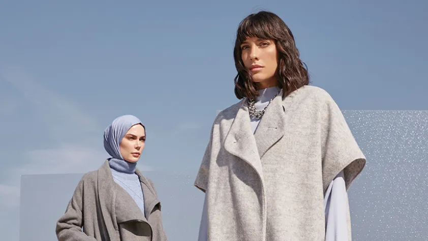 Two people modeling Modanisa clothes in front of sky blue background
