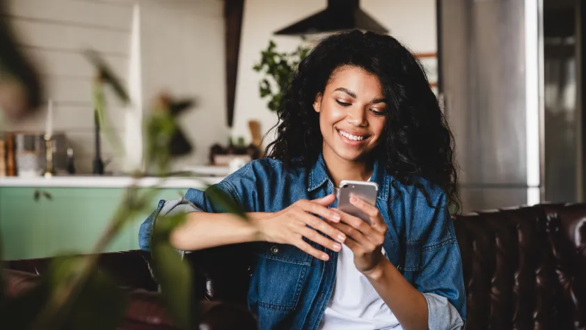 Person sitting on a brown couch, wearing a white t-shirt and blue denim shirt. They are interacting with an ad that clicks to WhatsApp on their phone.