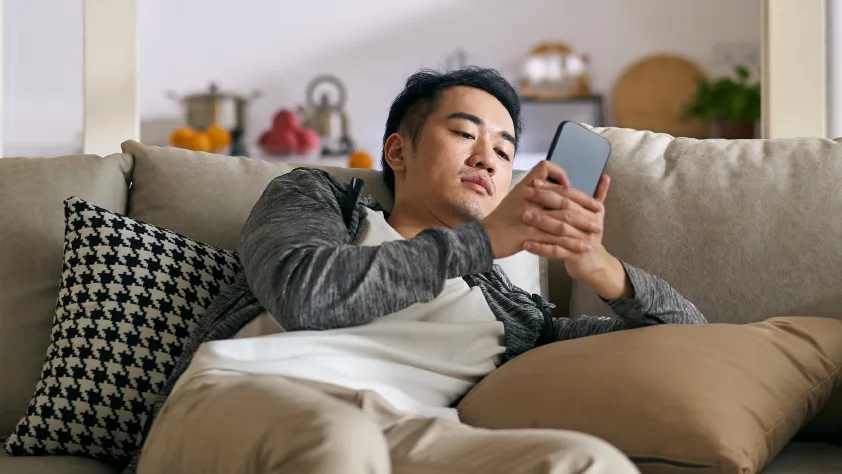 Person sitting on couch in living room. They are wearing a white t-shirt and a gray jacket while connecting with a sales and support team through WhatsApp.