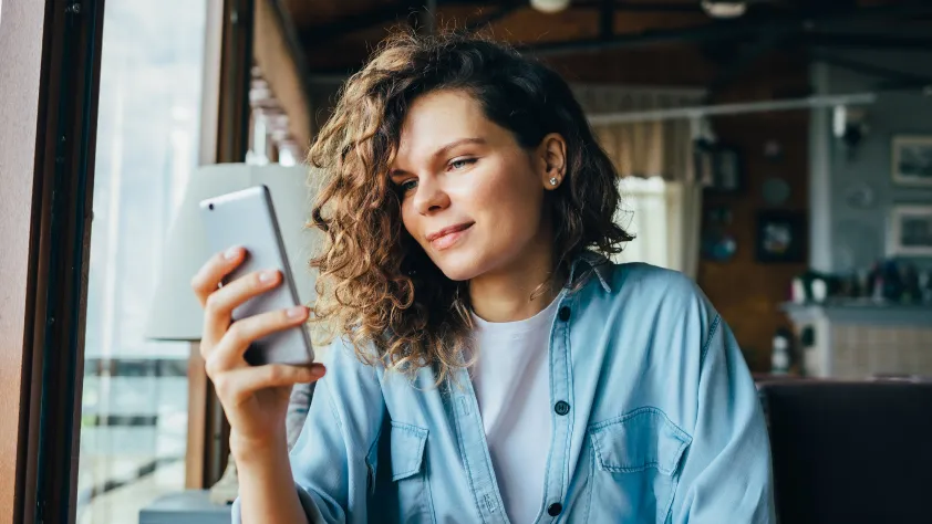 Person sitting by window in home while chatting with a business on their phone via WhatsApp