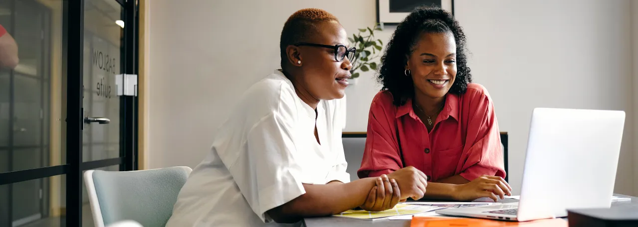 Two people sitting in a meeting room while looking at a presentation on their laptop
