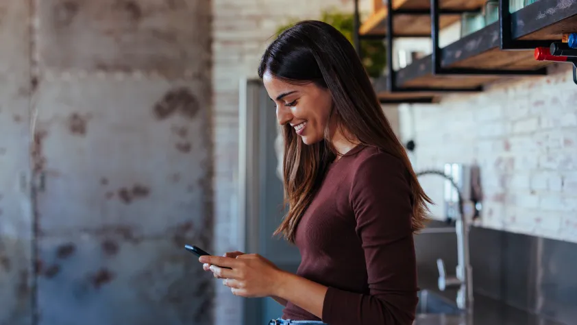 Person standing in kitchen, leaning against the counter while smiling and reading a WhatsApp business message on phone.