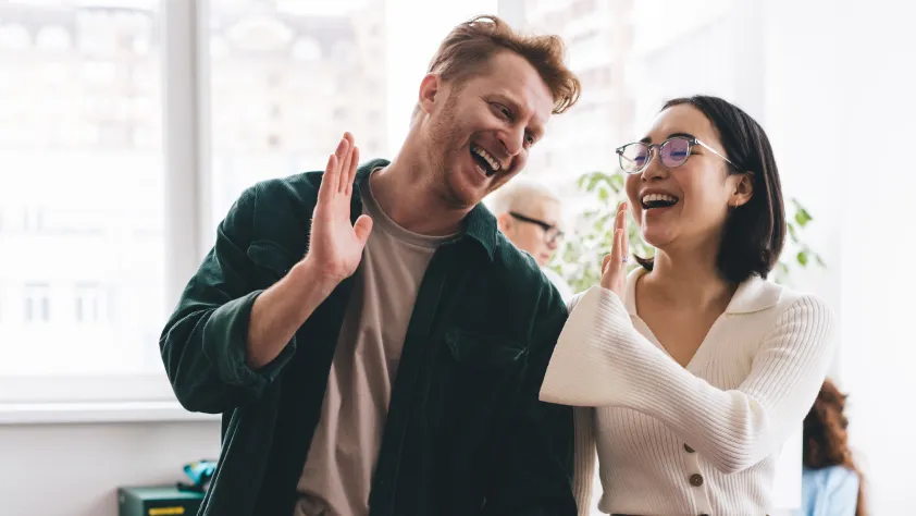 Two colleagues sitting next to each other and laughing while going in for a high five