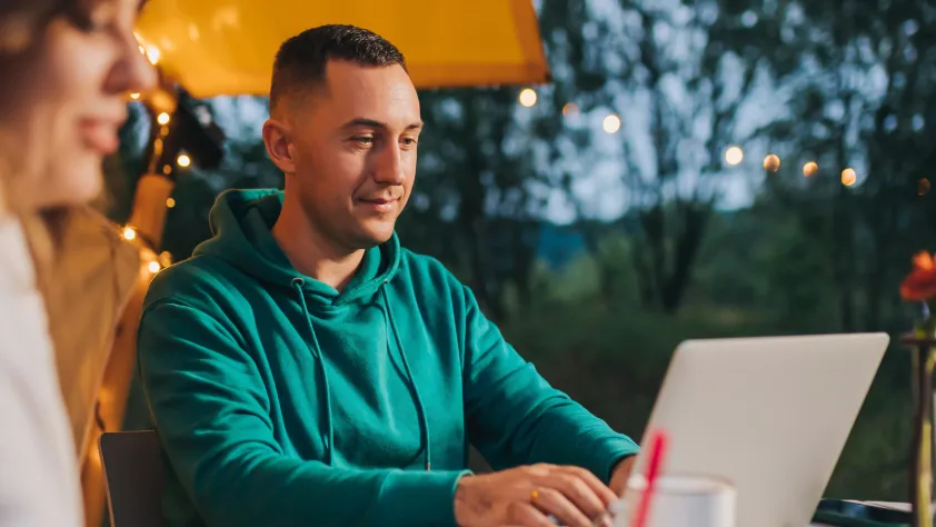 Person sitting on outdoor patio in the evening. They are wearing a green sweatshirt and working on laptop.
