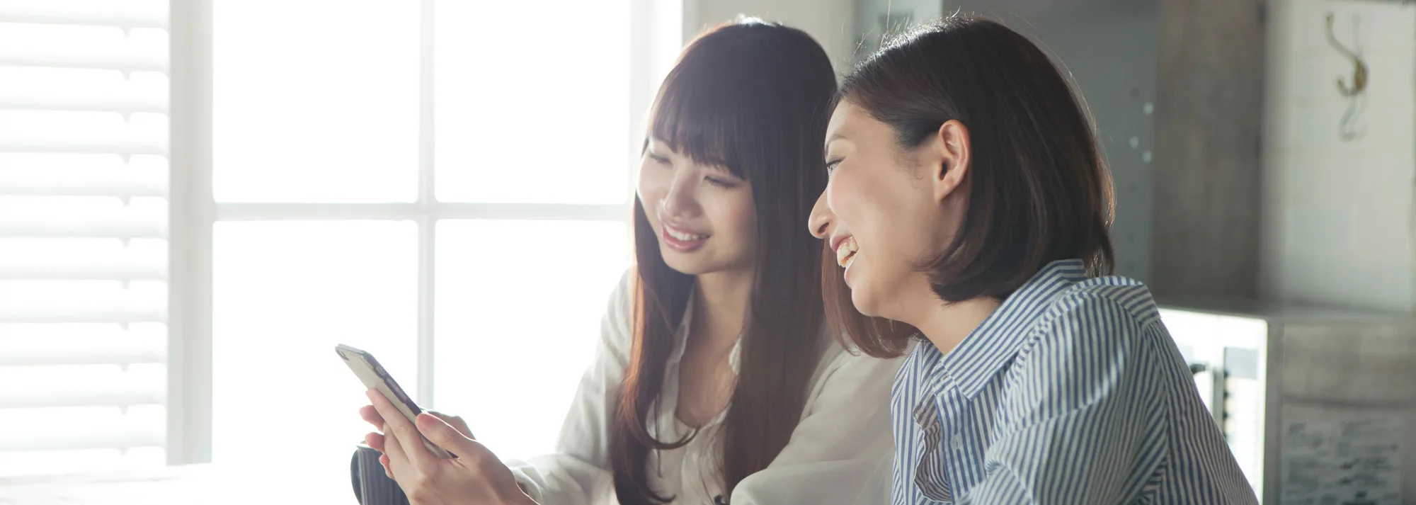 Two people sitting next to each other and smiling while looking at one of their phones