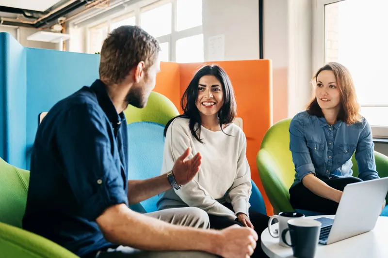 A man and two women sitting on chairs in an office talking to each other