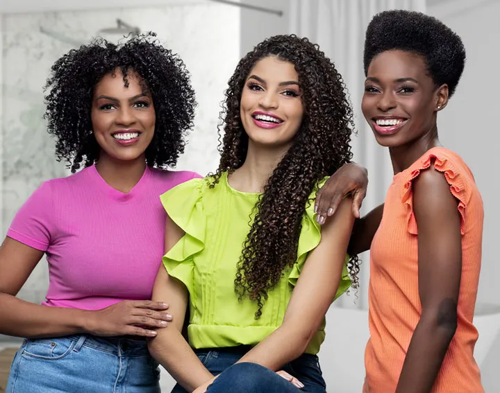 Tres mujeres sonrientes vestidas con blusas de colores.