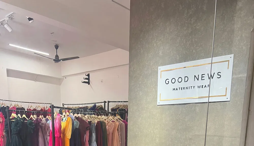 Logotipo de Good News Maternity Wear en la pared junto a una sala repleta de vestidos