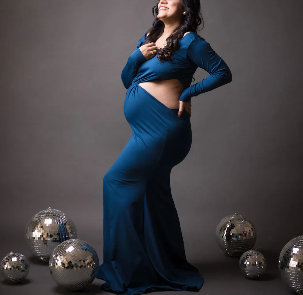 Embarazada con un elegante vestido azul, rodeada de bolas de espejo en el suelo