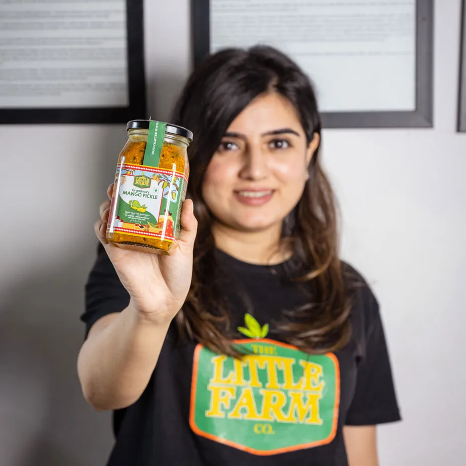 A woman in the background holding up a jar of pickles in the foreground