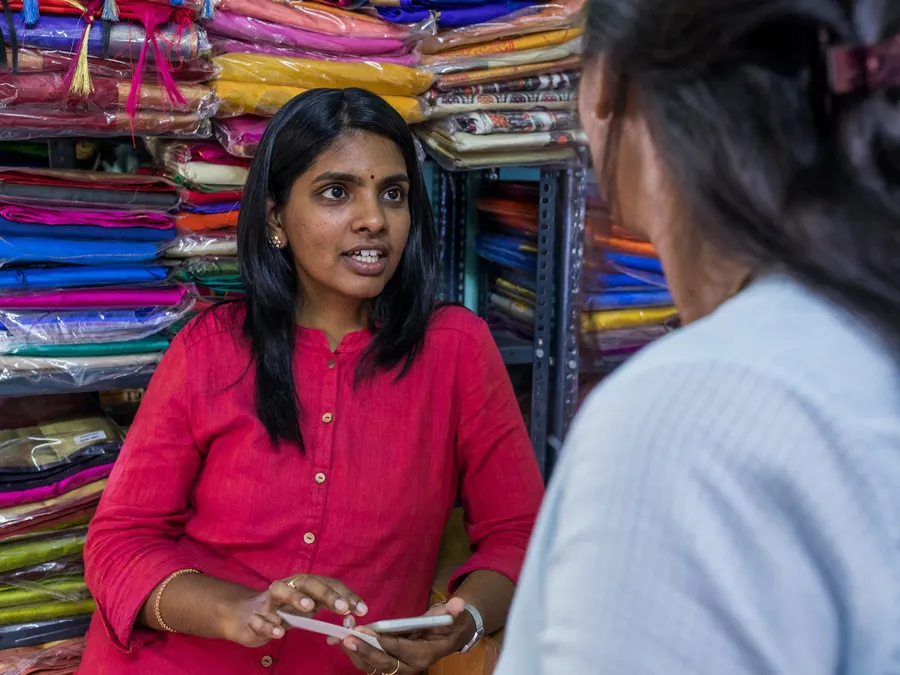 Two women talking to one another in front of a storage rack that is full of fabric