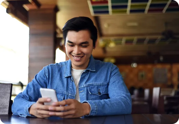A smiling man sitting at a counter looking at his phone