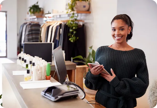 A smiling woman behind a service counter, holding a tablet