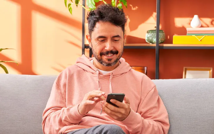 Person sitting on couch smiling at and scrolling on phone