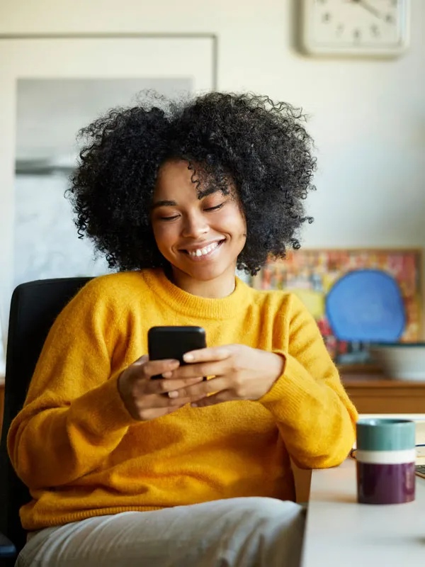 Una mujer sonriendo y mirando el teléfono sentada en su escritorio