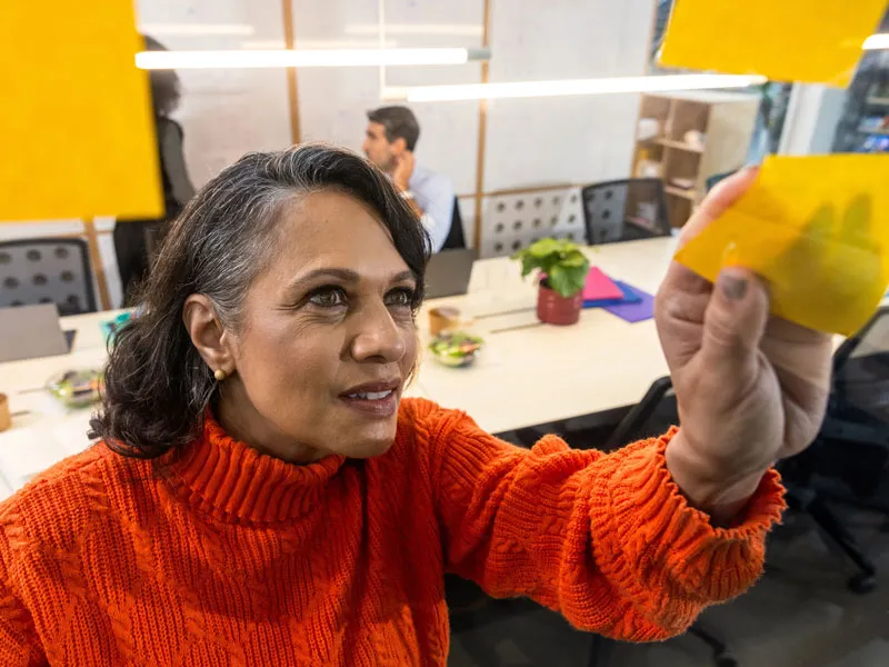 Woman in an office adding a sticky note to a wall