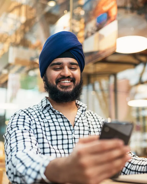 Un homme portant un turban bleu et une chemise à carreaux sourit en regardant son téléphone