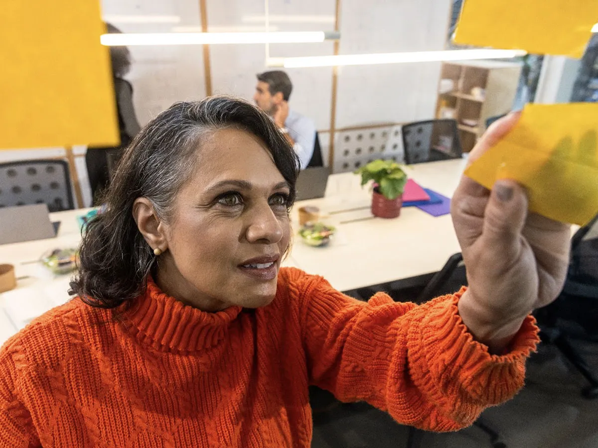 A woman in an office adding a post-it note to an unseen surface