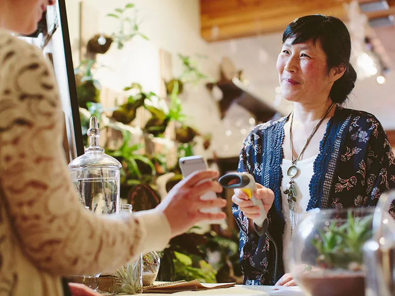 A cheerful cashier scanning a customer's phone at the checkout counter.
