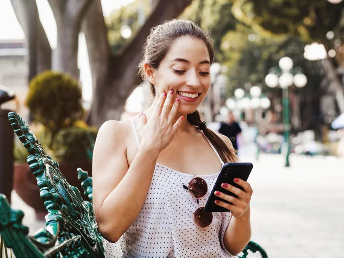 A woman standing at a counter, using her smartphone. A cashier across from her smiling from behind a wooden counter with a cash register and macarons