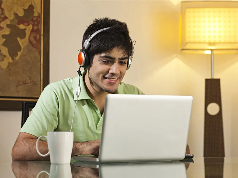 A man with a headset sitting at a desk smiling at his computer