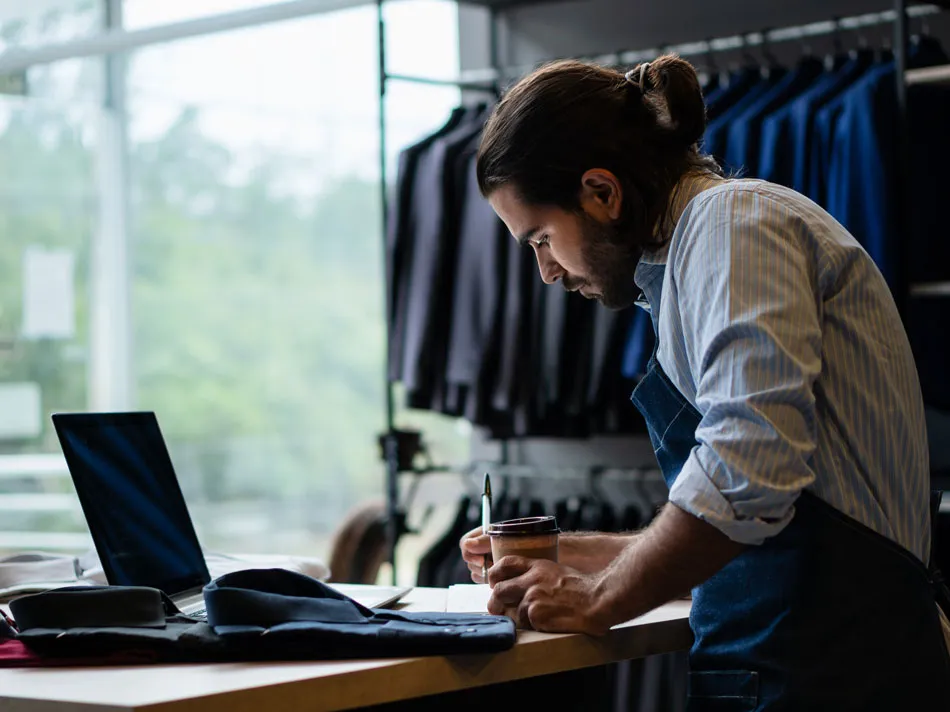 A man behind a desk with a laptop, jotting down notes