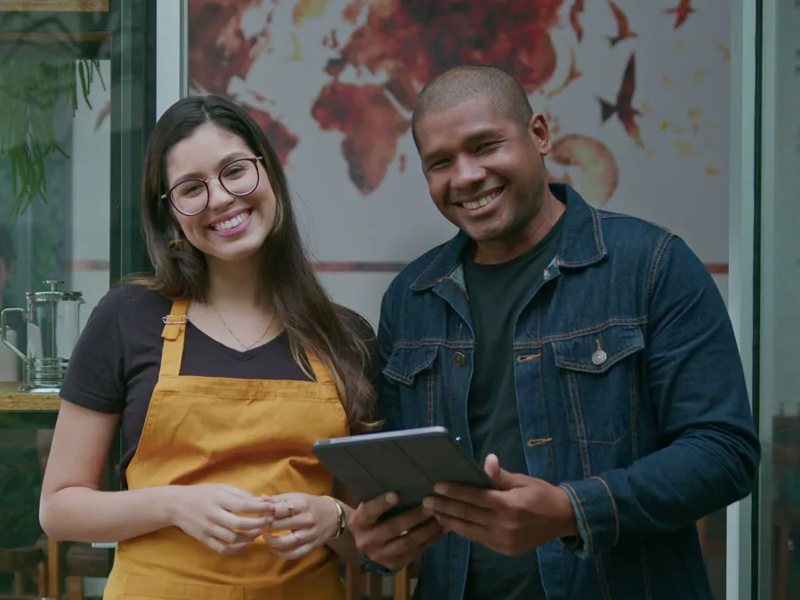 Two people smiling in a business, one holding a tablet