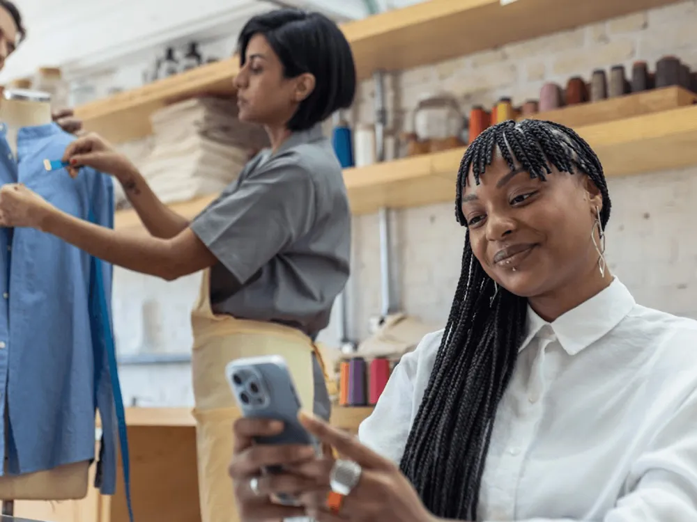 Two women working in an office, one looking at her phone and the other helping a customer