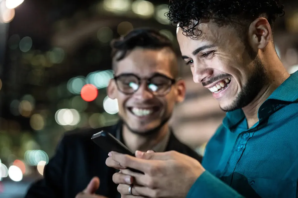 Two men smiling and looking at one of their phones