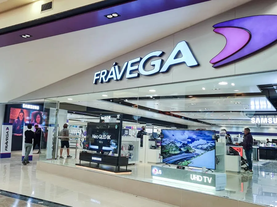 An image of a Fravega company storefront with TVs on display behind tall glass walls and customers walking in