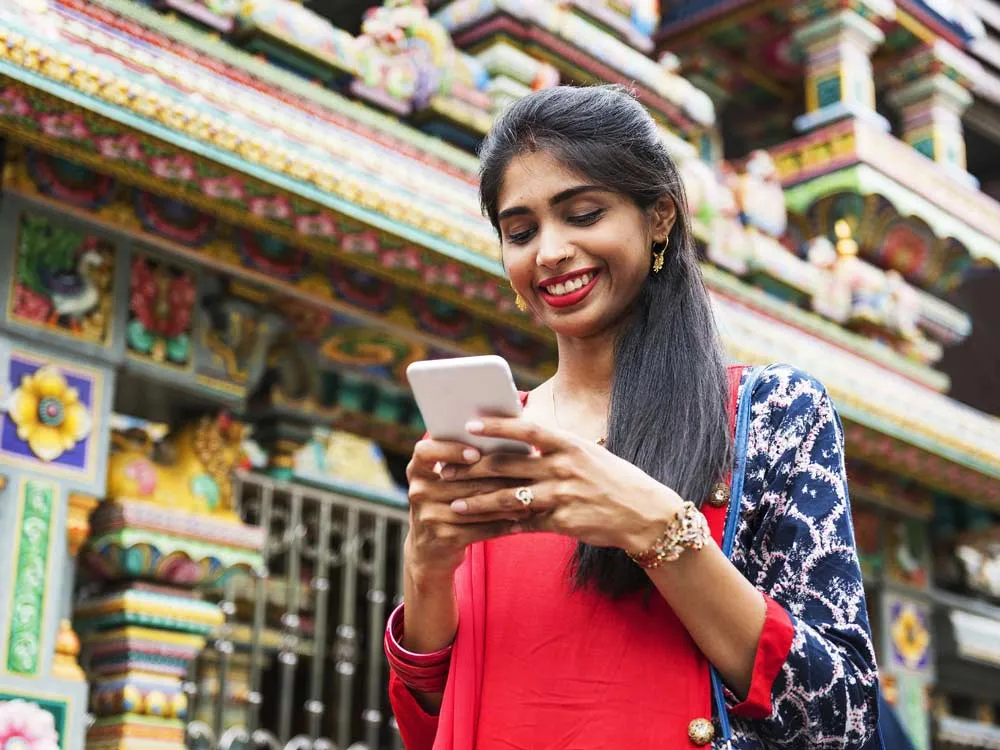Une femme en extérieur qui sourit en regardant son téléphone portable